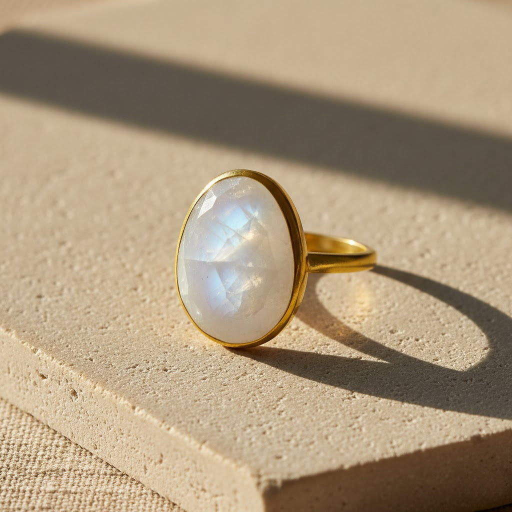Rainbow moonstone oval ring bezel set in gold vermeil displayed on a neutral stone surface, featuring a luminous June birthstone with natural iridescence. Minimalist moonstone jewelry designed for everyday wear, stacking, and meaningful gifting. Handmade gemstone ring perfect for birthdays, anniversaries, Valentine’s Day, or elegant modern styling.