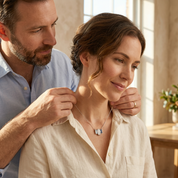 Man adjusting a necklace on a woman in a bright room with natural light.