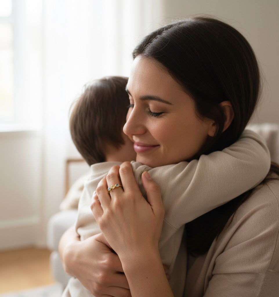 Loving mom hugging her young child while wearing a dainty three-stone birthstone ring on her hand, each bezel-set gemstone representing her children and family. This sentimental mom birthstone ring in gold makes a meaningful Mother’s Day gift, push present, or birthday gift for moms who love minimalist, personalized jewelry and family keepsakes, perfect for everyday wear to celebrate kids and capture special memories together.