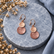 Blush Pink and Rose Gold hammered double disc earrings displayed on gray stone
