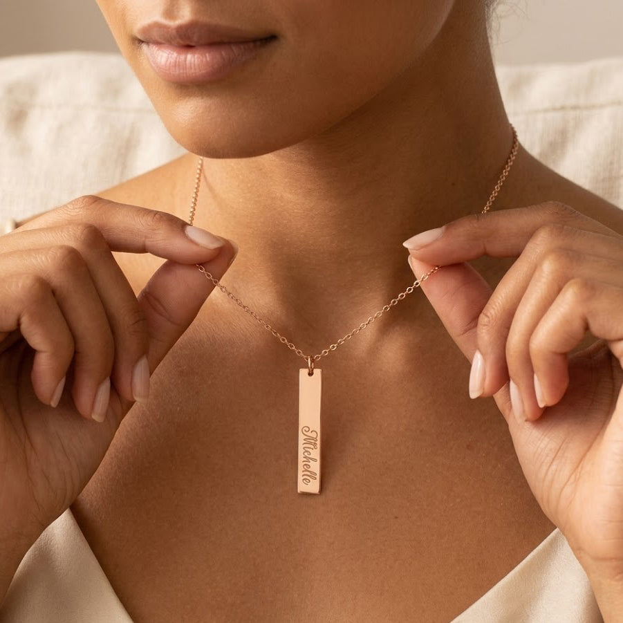 Model holding a sterling silver vertical bar necklace engraved with custom coordinates