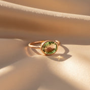 Warm sunrise lighting highlights a delicate oval bezel-set green gemstone ring in 14k rose gold vermeil, displayed on soft champagne satin for an elegant, minimalist aesthetic. This dainty October birthstone style makes a meaningful personalized gift for mom, daughter, sister, or best friend. Crafted in .925 sterling silver with optional gold finishes, this modern gemstone ring is perfect for stacking, everyday wear, and special occasion gifting.
