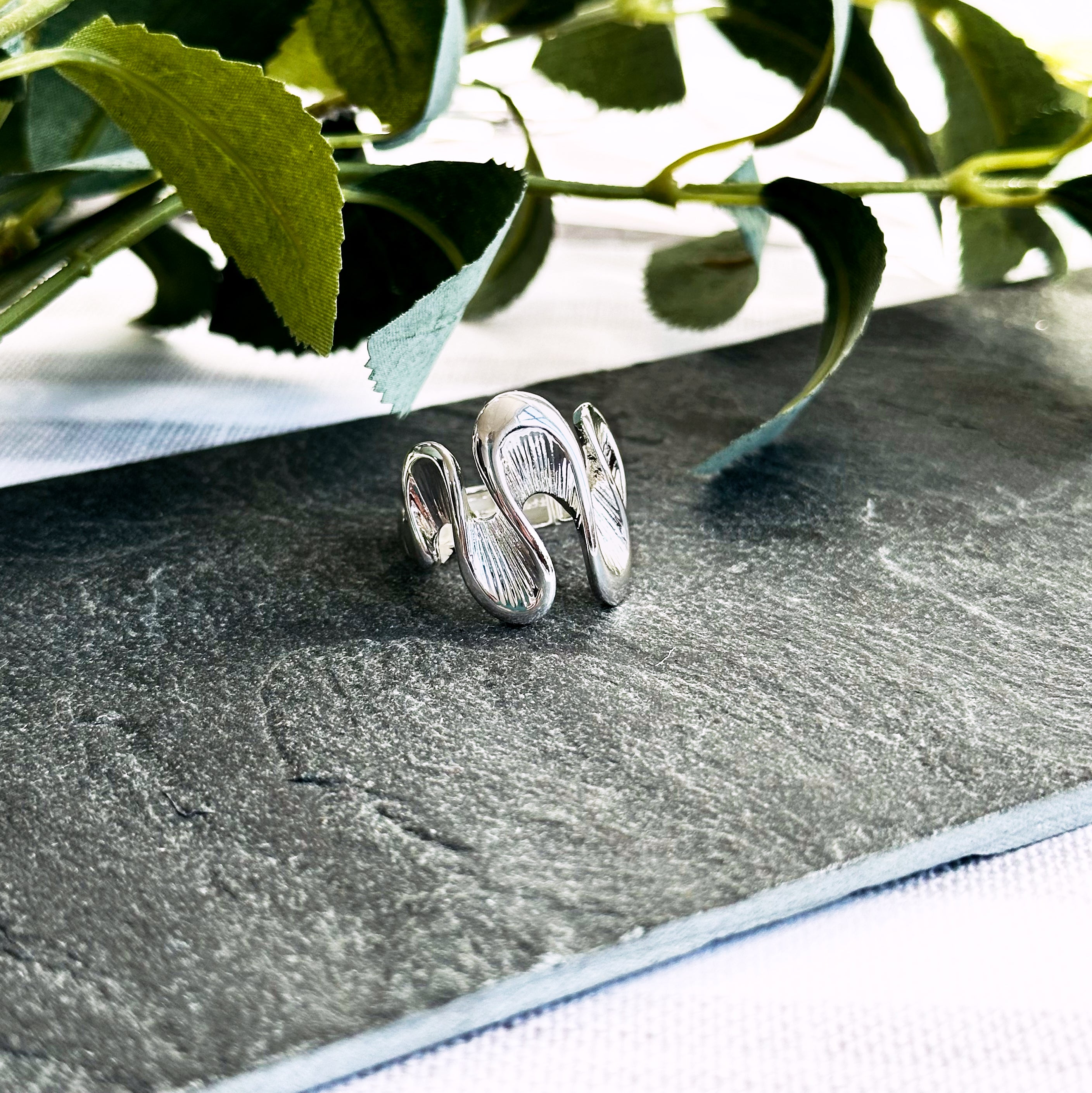 Silver Waves ring rests on a flat dark stone with leaves in the background