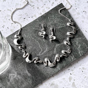 Silver wave necklace and earrings set displayed on dark stone for artistic boho jewelry styling