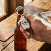 Hand using custom bottle opener keychain to open beer bottle. Functional personalized keychain gift for beer lovers.