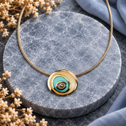 Boho turquoise and gold evil eye spiral pendant necklace displayed on gray stone
