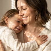 Mom wearing personalized birthstone necklace while holding child

