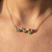 Minimalist mom birthstone necklace featuring a curved zigzag row of bezel-set gemstones, shown in a dainty yellow gold finish.