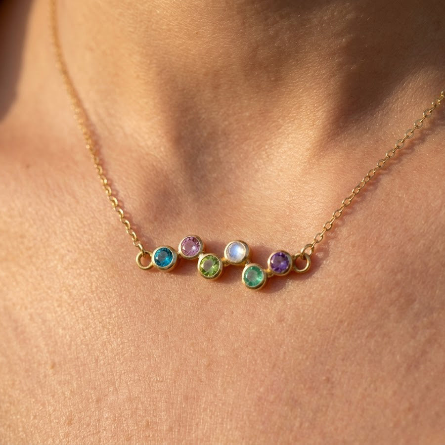 Minimalist mom birthstone necklace featuring a curved zigzag row of bezel-set gemstones, shown in a dainty yellow gold finish.