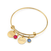 Gold bangle bracelet with engraved disks in handwriting script and garnet and kyanite birthstones. 