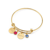 Gold bangle bracelet with engraved disks in handwriting script and garnet and kyanite birthstones. 