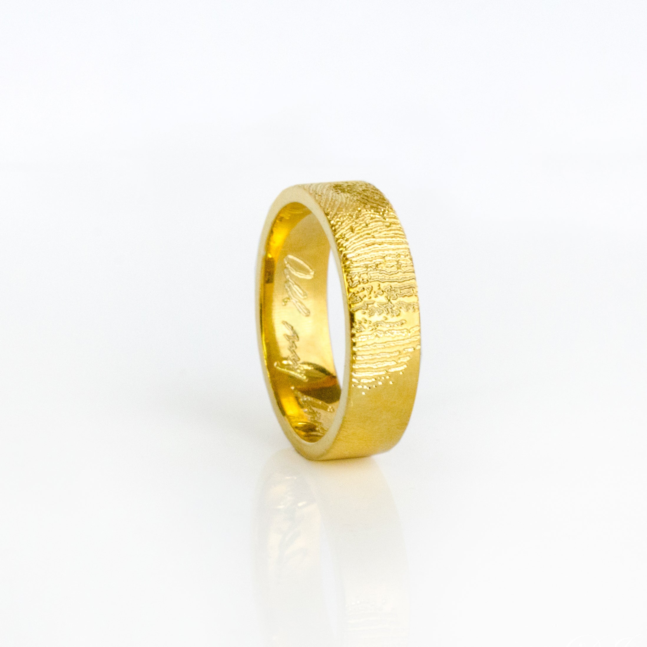 A gold wide band ring engraved with a fingerprint lies on its side. 6mm engraved fingerprint band, custom handwriting ring, sterling silver jewelry, gold wide band, rose gold personalized ring, engraved names, dates, coordinates, photo engraving, meaningful gift, stylish accessory, unique keepsake, inside or outside engraving, US sizes 4-13. Gift for her, gift for him, memorial gift, commemorative gift, gift for fiance, gift for husband, gift for wife, gift for girlfriend, gift for boyfriend, silver