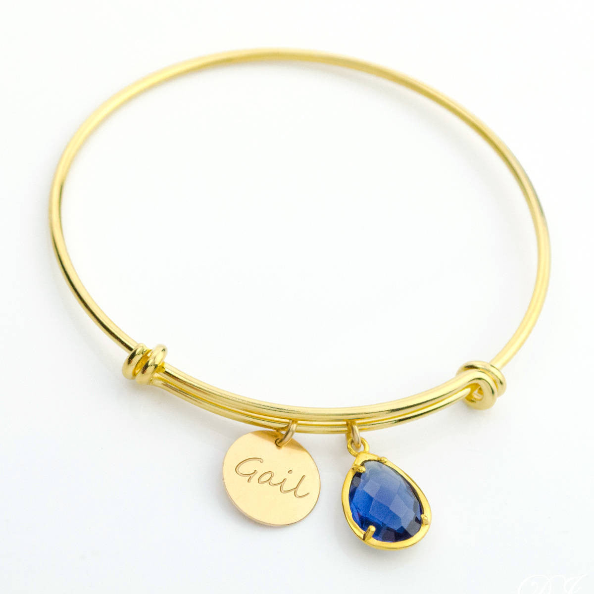 Gold bangle featuring 13mm disk engraved with script font and a prong set kyanite birthstone.