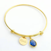 Gold bangle featuring 13mm disk engraved with script font and a prong set kyanite birthstone.
