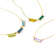Collection of three adira horizontal bar necklaces with engraved secret message. One gold filled necklace with peridot, kyanite, and blue topaz. One gold gilled necklace with citrine and green onyx birthstones and 1 gold filled necklace with purple amethyst.