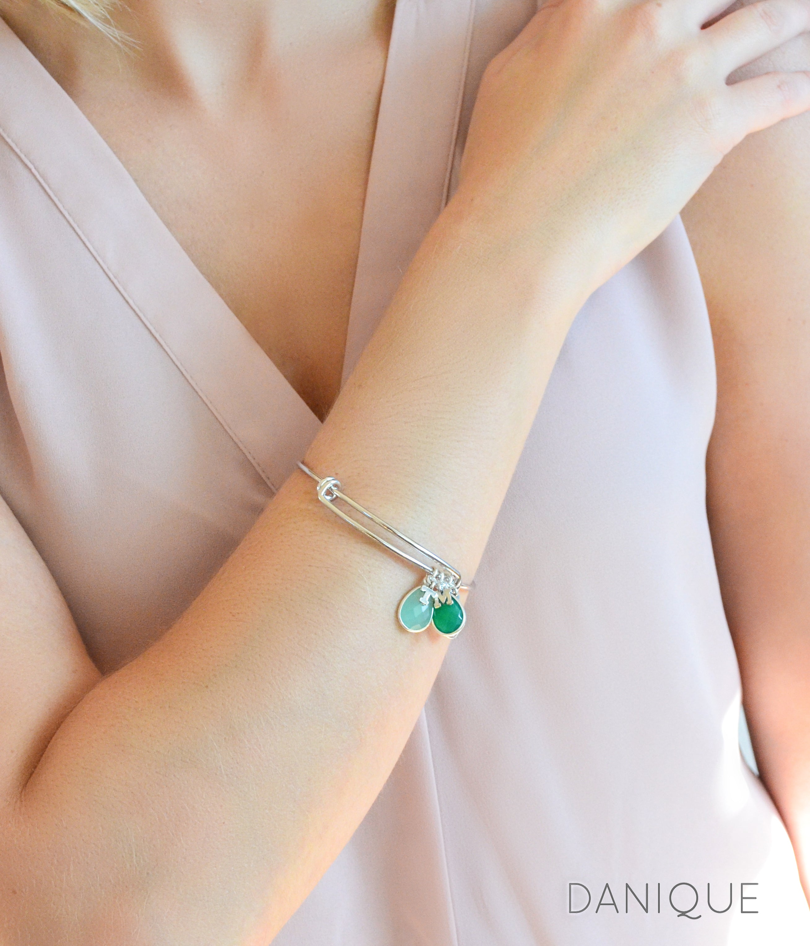 model in cream top is wearing a silver bangle bracelet with two initial charms letter charms and aqua chalcedony and green onyx birthstones. march birthstone, may birthstone, birthstone jewelry