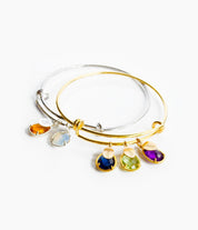 Silver bangle on the bottom with script initial name tags and citrine and moonstone birthstones. Gold bangle on top with classic names engraved with kyanite, peridot and purple amethyst birthstones.