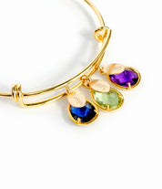 Gold bangle on top with detailed view of classic names engraved with kyanite, peridot and purple amethyst birthstones.