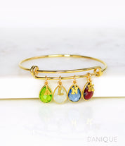 Gold bangle with plain style initial charms, letter charms and peridot, moonstone, kyanite and garnet birthstones. august birthstone, june birthstone, september birthstone, january birthstone 