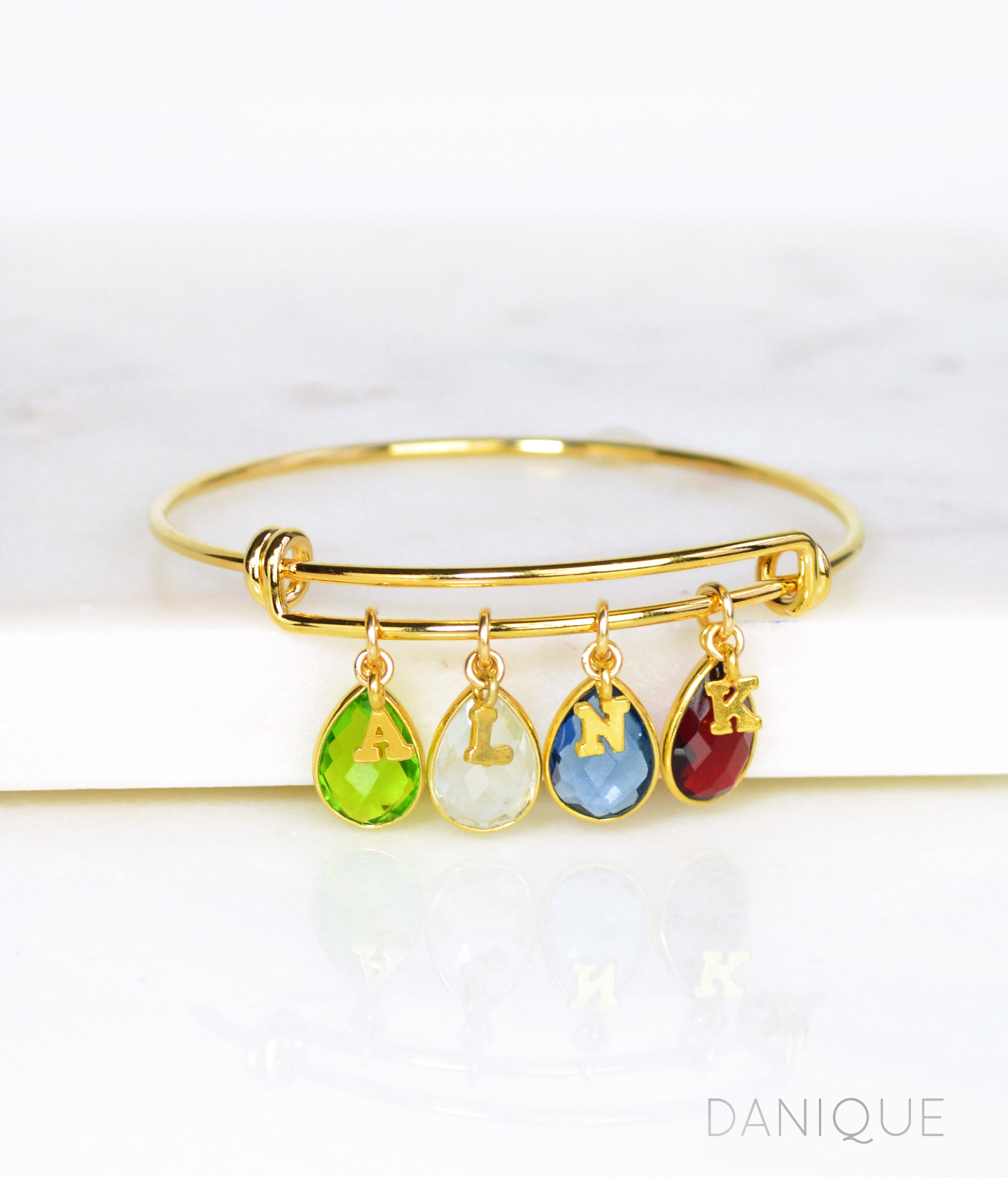Gold bangle with plain style initial charms, letter charms and peridot, moonstone, kyanite and garnet birthstones. august birthstone, june birthstone, september birthstone, january birthstone 