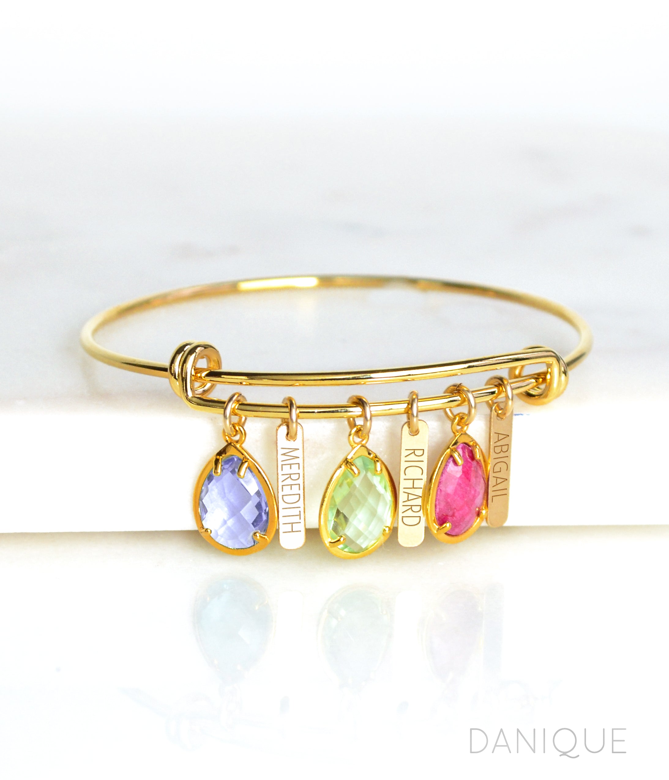 Gold birthstone and engraved name bar bangle bracelet with purple amethyst, peridot, and ruby birthstones.