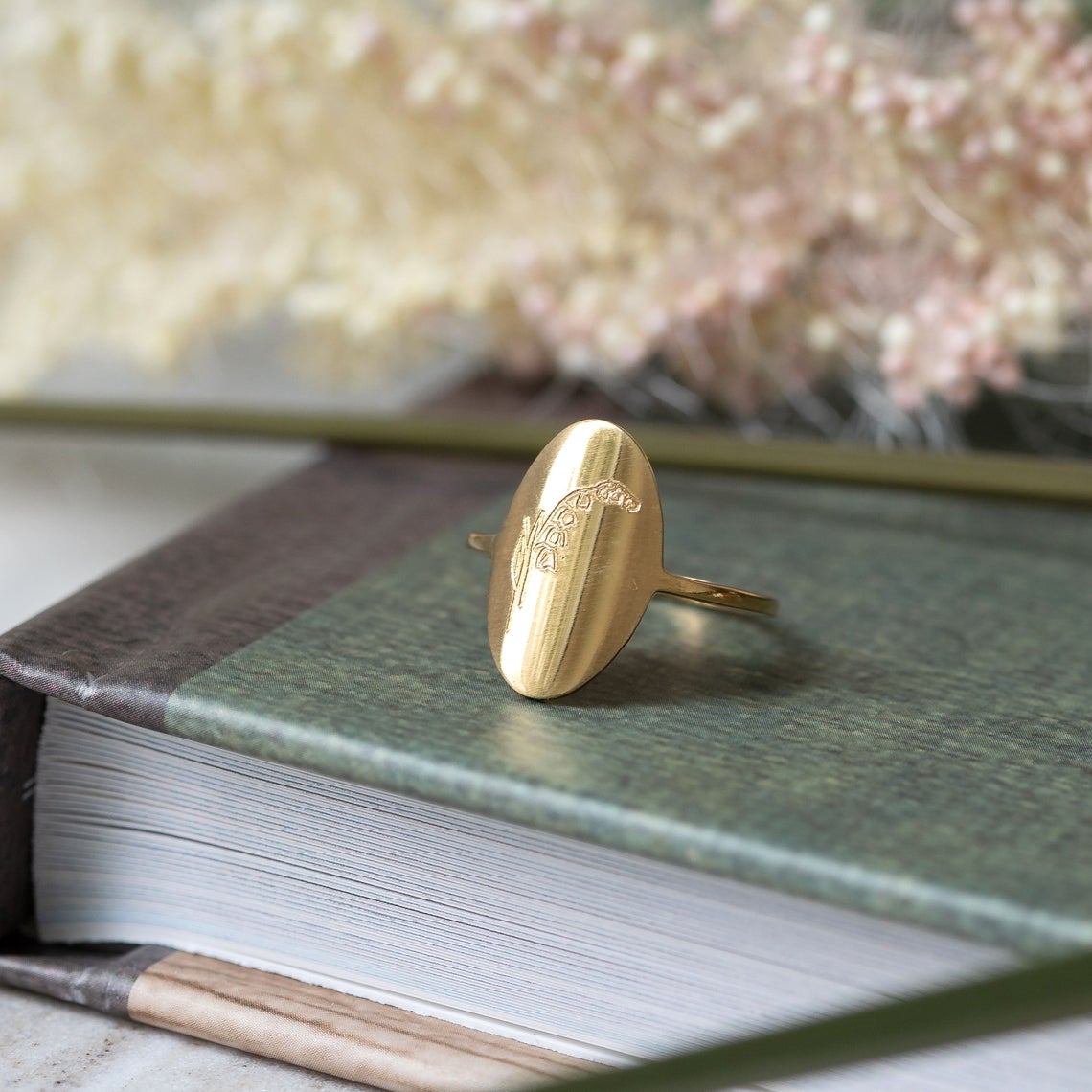 single gold engraved birth flower ring displayed on book
