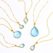 Shop our blue topaz necklace collection available in large, medium and small teardrops, prong set teardrop, prong set diamond, large and medium rounds on white background. Choose from satellite or cable chain. December birthstone. 