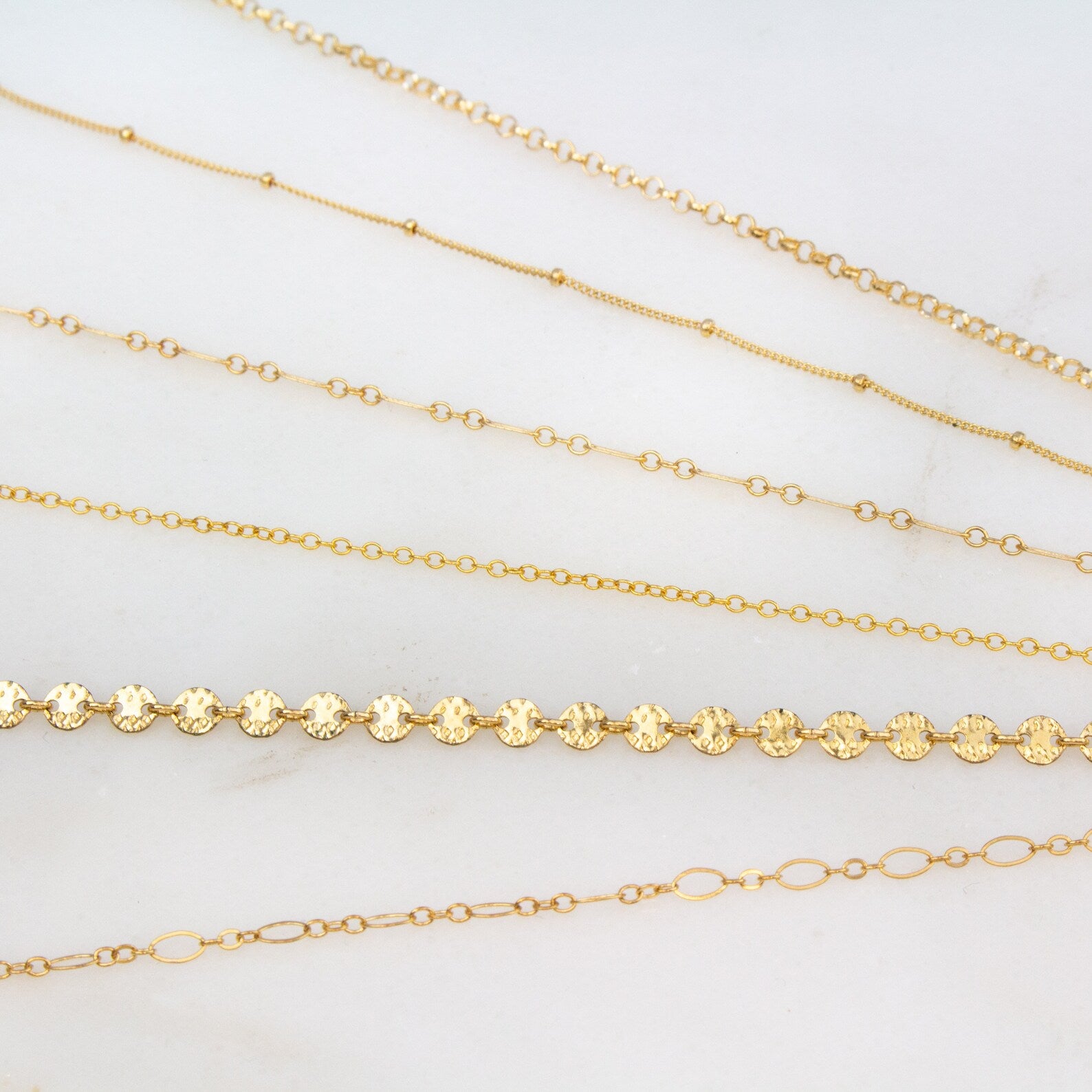 Detailed view of the gold filled rolo, satellite, box, cable, coin and loop anklets.