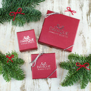 3 red Danique Jewelry boxes with silver bows rest on a white background with flowers along the edges of the image. Each piece comes in a gift-ready box ready to be handed off to the recipient immediately, or to be delivered directly to them.