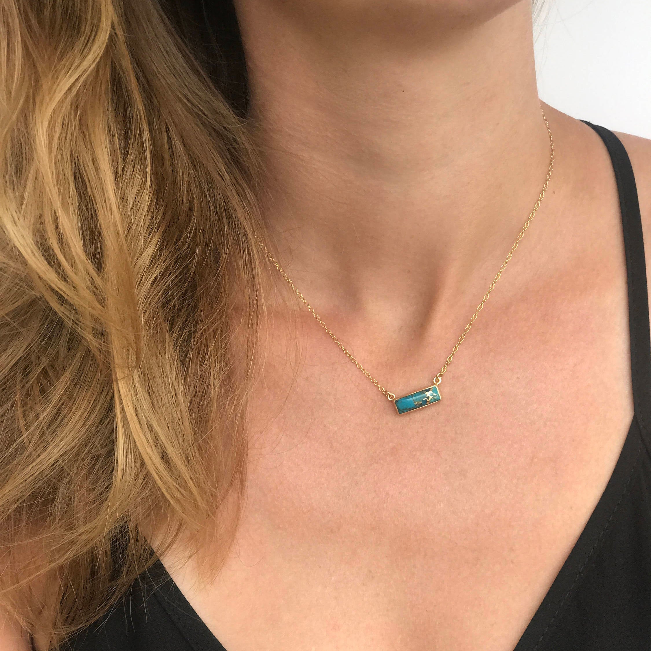Model in black top is wearing a single gold filled cable chain copper turquoise horizontal adira bar necklace with white background. december birthstone