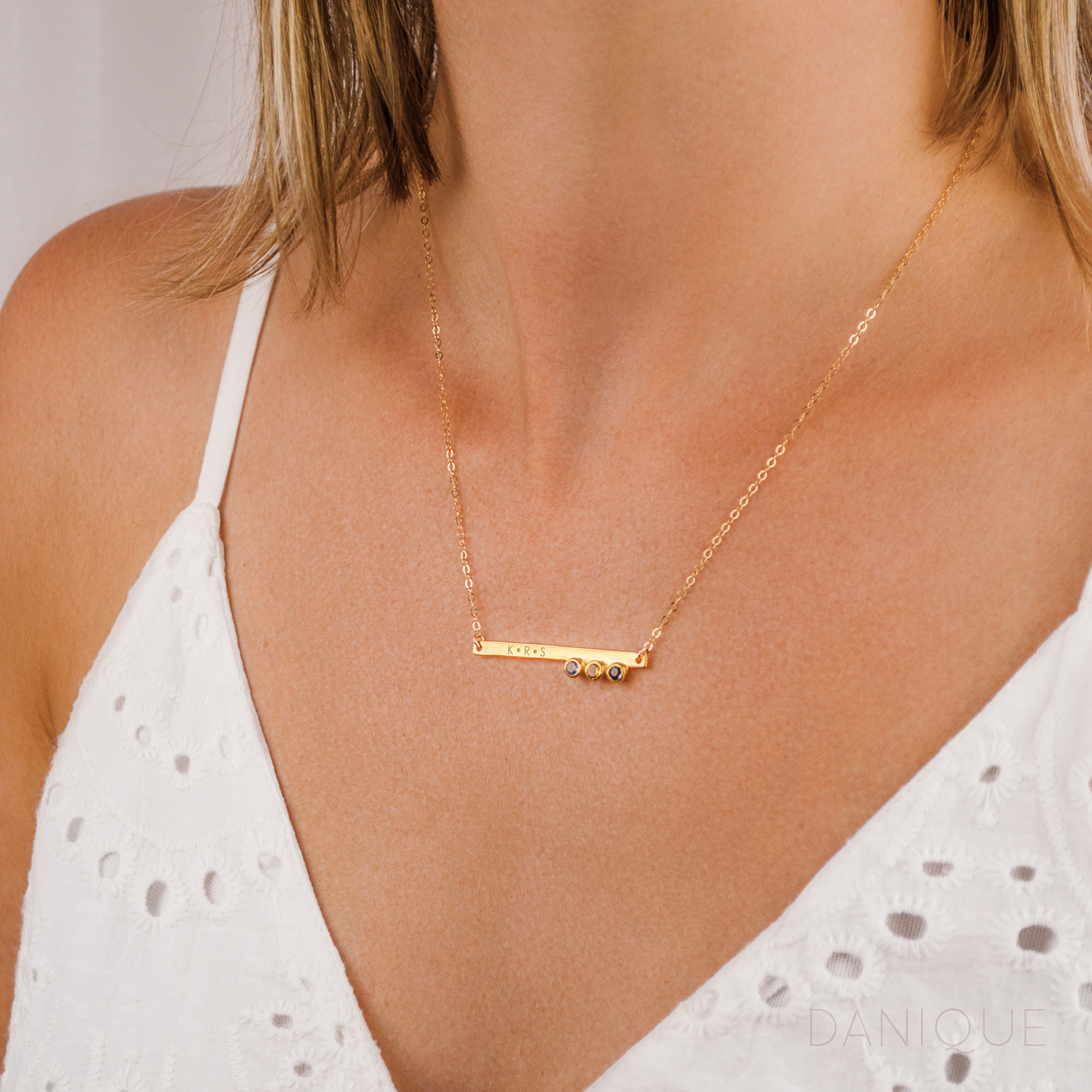 Model in white top is wearing Gold plated skinny bar necklace with initials engraved with the purple amethyst, citrine and iolite birthstones. 