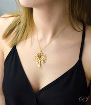 Model in black top wearing gold filled swirly tree necklace with engraved oval name tags and pink chalcedony dyed ruby and opalite birthstones. 