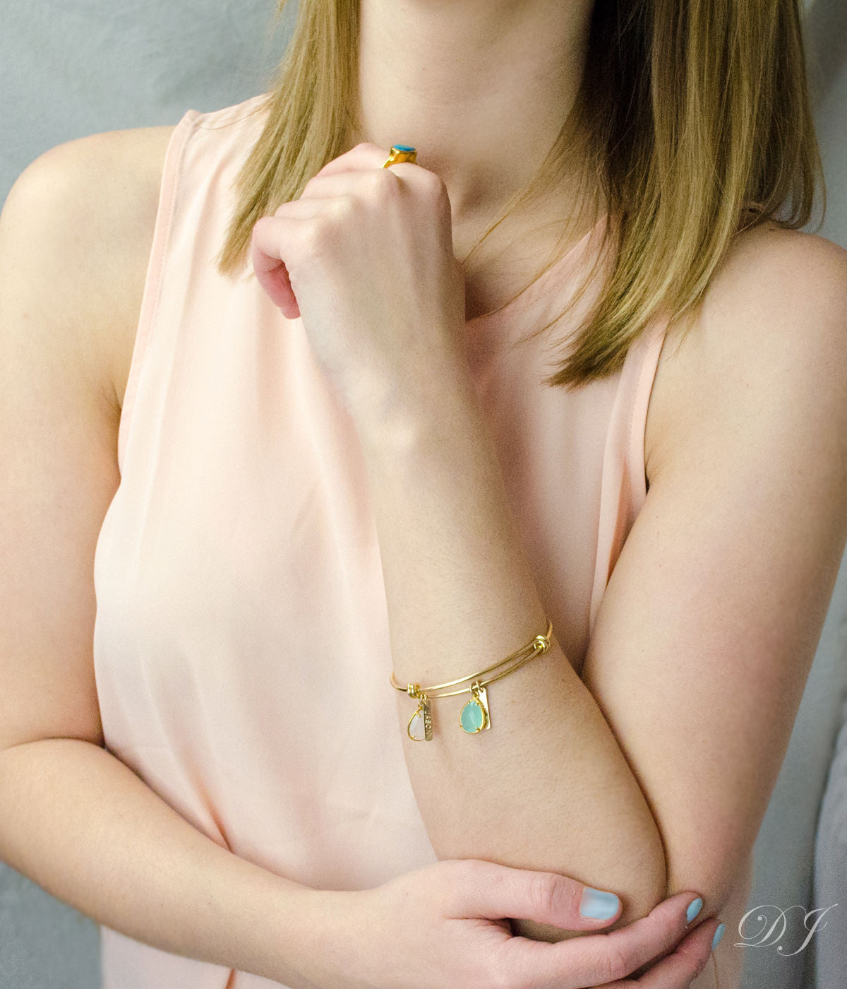 Model in cream colored top is wearing a single gold bangle with engraved name bars and pink chalcedony and aqua chalcedony birthstones.