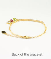 Back of gold filled bracelet has been engraved with names in script font. Peridot, ruby and clear birthstones are shown.