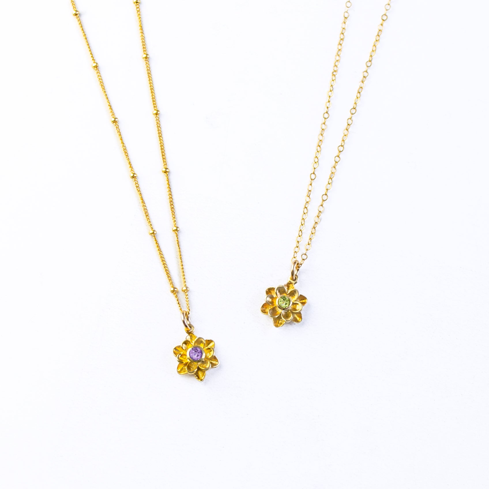 Large gold filled floral flower bloom necklaces. Left features a satellite chain with purple amethyst birthstone. The right necklace is on a cable chain with peridot birthstone. 