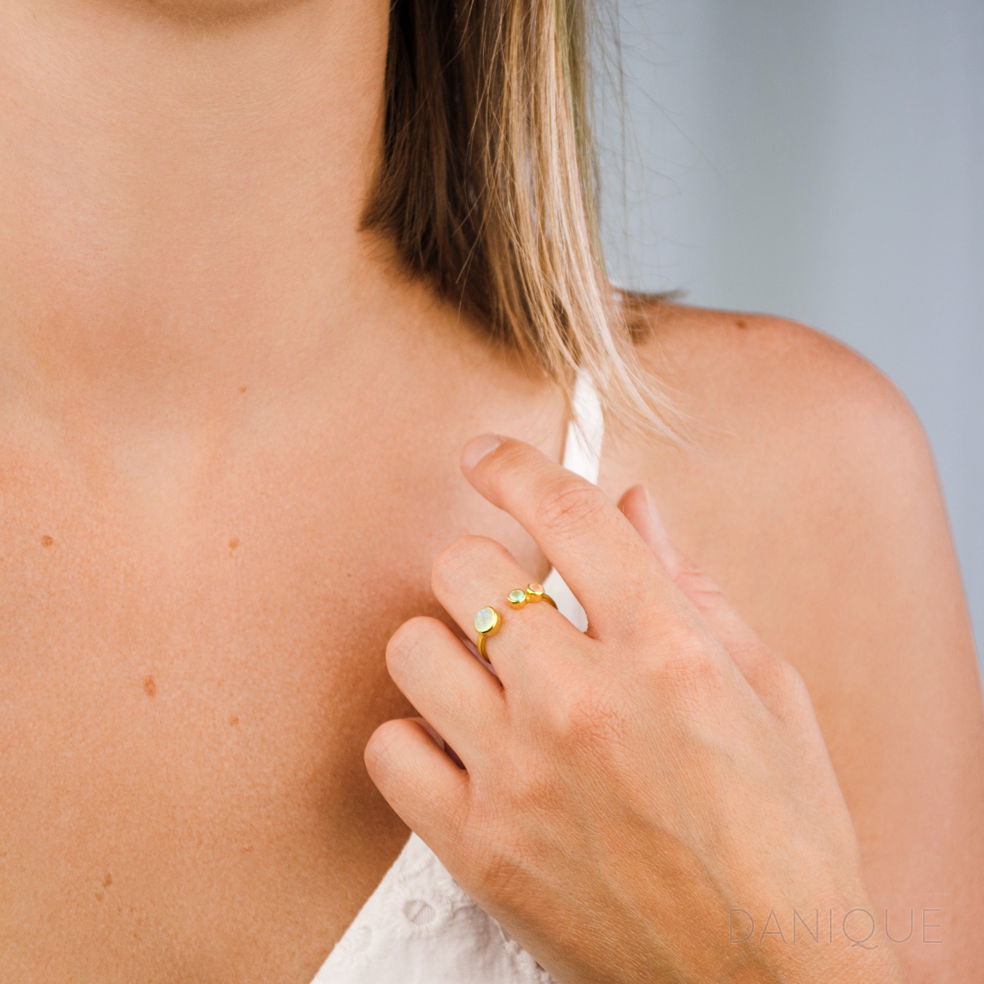 Model in white top is stylishly wearing a gold filled mother's and children's birthstone ring with moonstone, aqua chalcedony and pink chalcedony birthstones. 