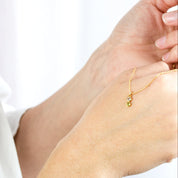 Model is holding a gold filled satellite chain with 2 birthstones on the vertical bar necklace including peridot and clear quartz, the birthstones for August and April respectively.
