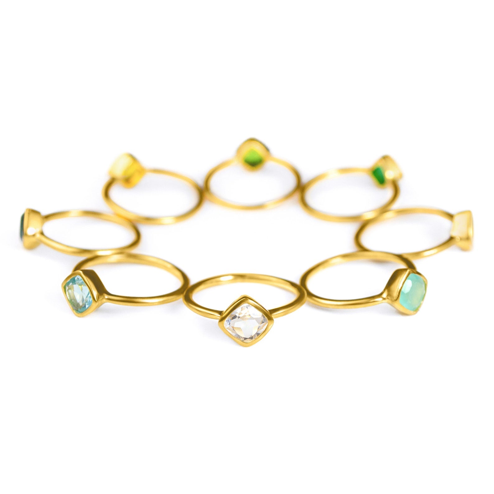 Collection of diamond shape bezel set gold plated rings with green onyx, peridot, citrine, blue quartz, clear quartz and aqua chalcedony birthstones on a white background
