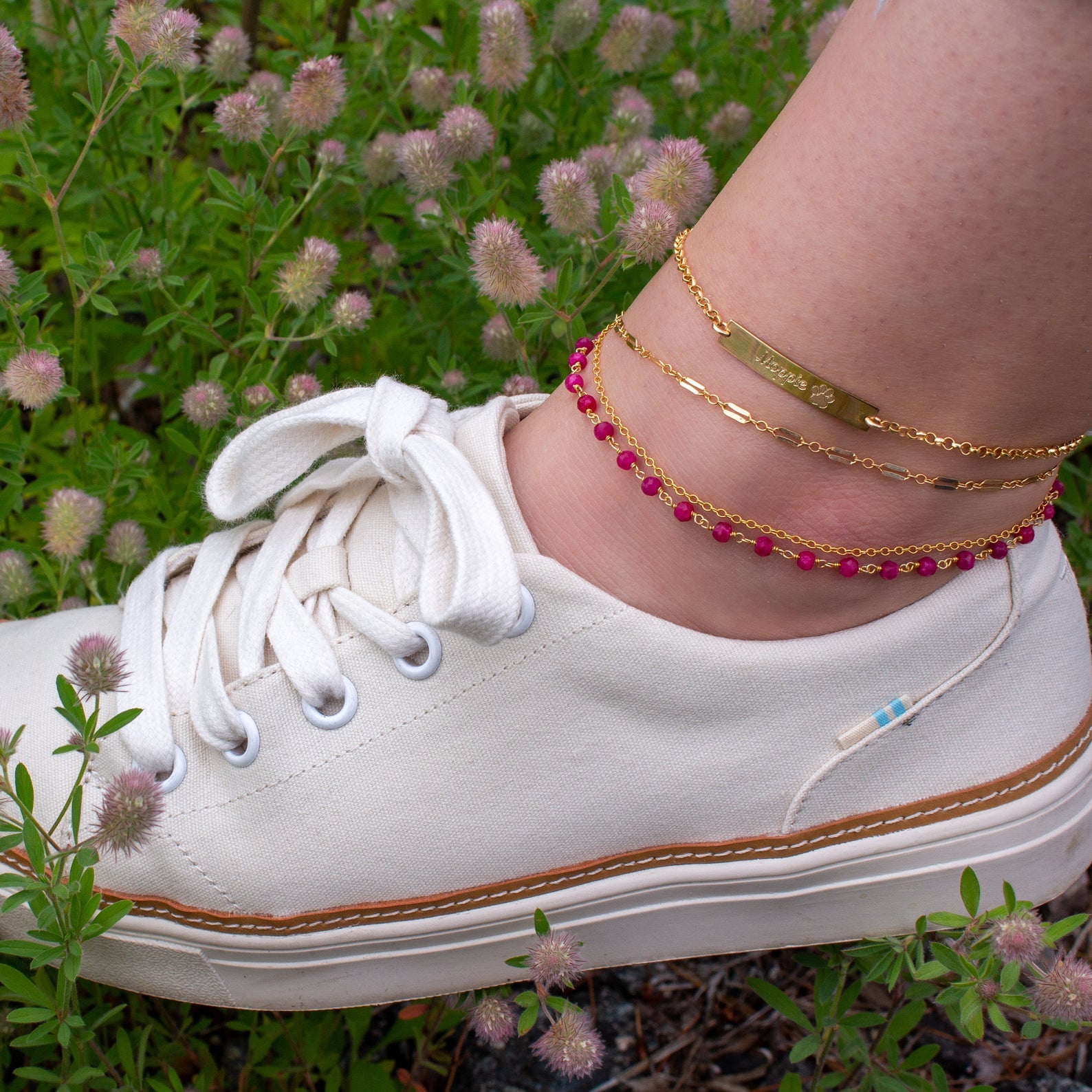 Model wearing four anklets from our collection all gold filled including the ruby wire wrap anklet, pet paw print bar, cable and box chain anklets. Perfect for layering!