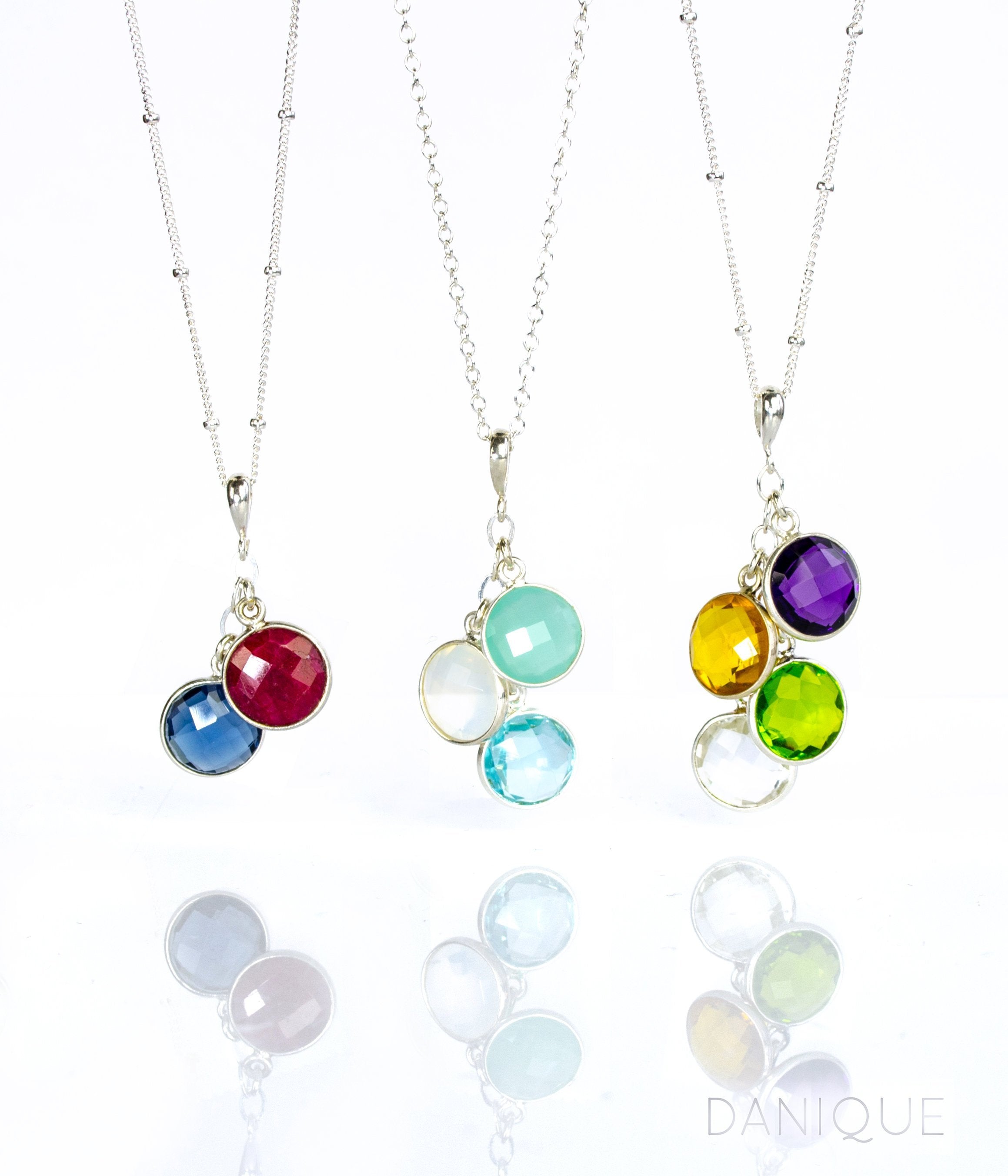Three cascade silver round necklaces. First necklace features satellite chain with garnet and kyanite birthstones. Middle cable chain necklace has aqua chalcedony, moonstone and blue topaz. The third necklace has a satellite chain with purple amethyst, citrine, peridot and clear birthstones.