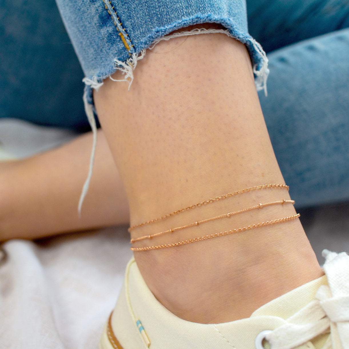 Model is fashionably wearing three rose gold filled anklets in the satellite, cable and rolo chain styles. 