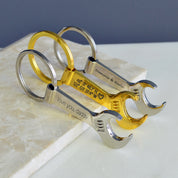 Three keychains, first silver tone wrench keychain engraved with special message. middle keychain Single gold toned wrench keychain with special GPS coordinates engraved and a heart emoji. last silver toned keychain with two names engraved. bottle opener keychain