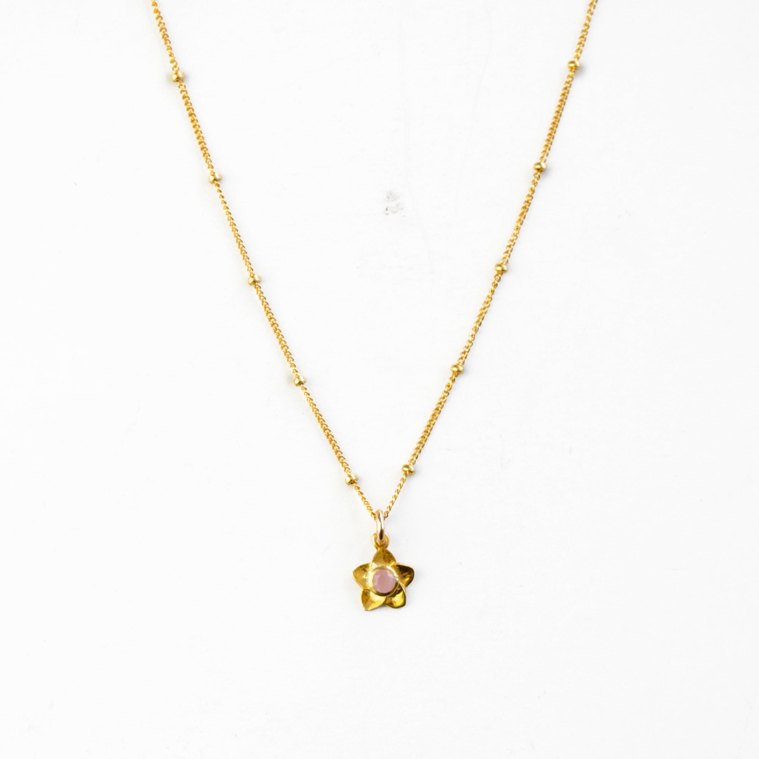 Single small flower bloom pink chalcedony birthstone necklace on a gold filled satellite chain with a white background. 