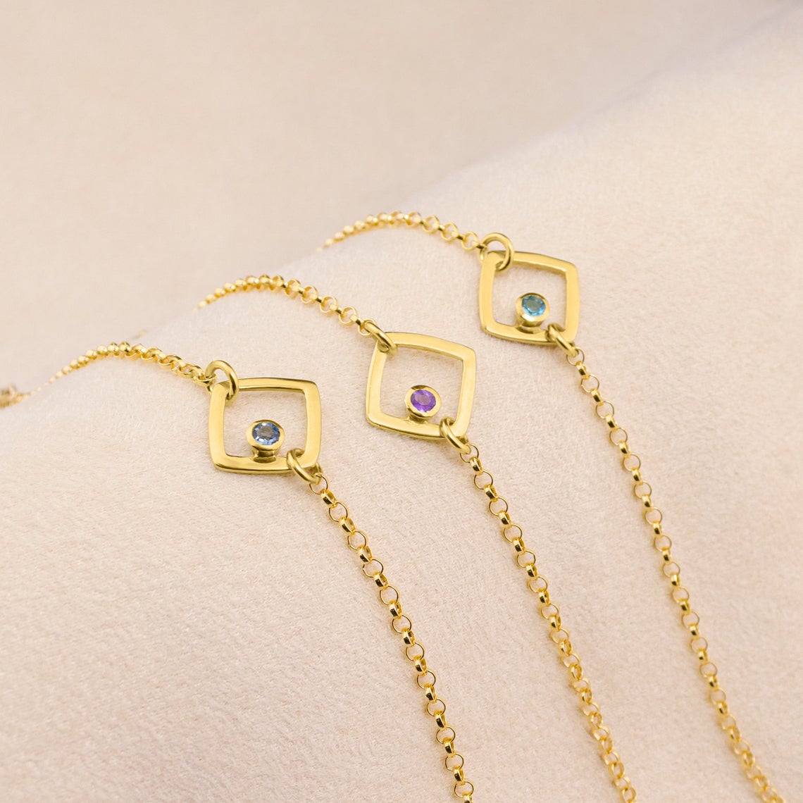 Series of three open square geometric bracelets with kyanite, purple amethyst and blue topaz birthstones. 