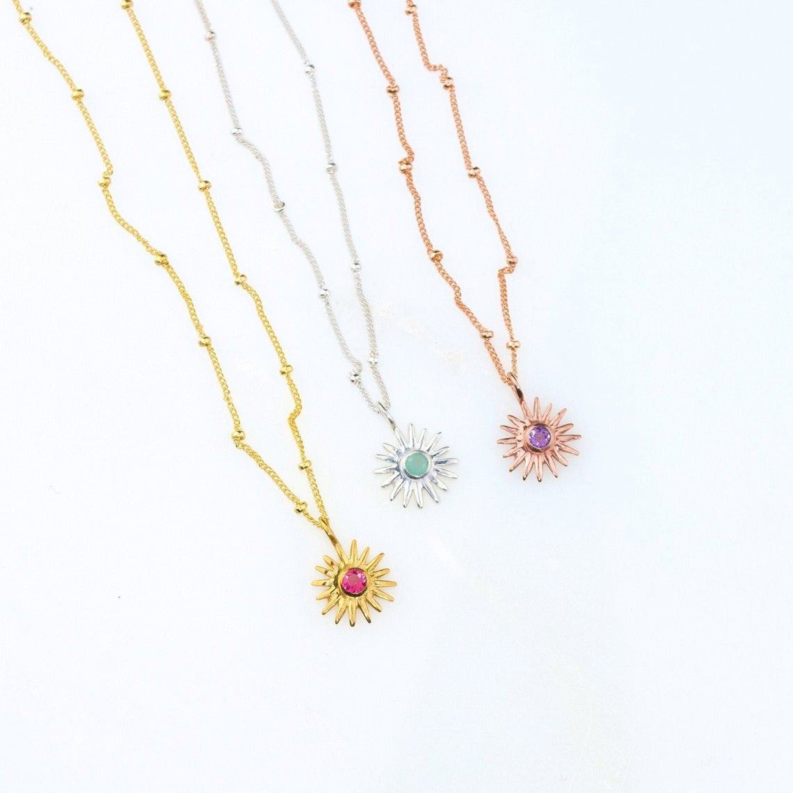 Dainty sunburst birthstone necklaces displayed in gold filled, sterling silver, and rose gold filled finishes, each featuring a sparkling center birthstone in a radiant sun design. Personalized minimalist jewelry perfect for everyday wear or gifting, available with all twelve birthstones for birthdays, Mother’s Day, Christmas, bridesmaids or best friend gifts. Ideal sentimental necklace for stacking or layering.