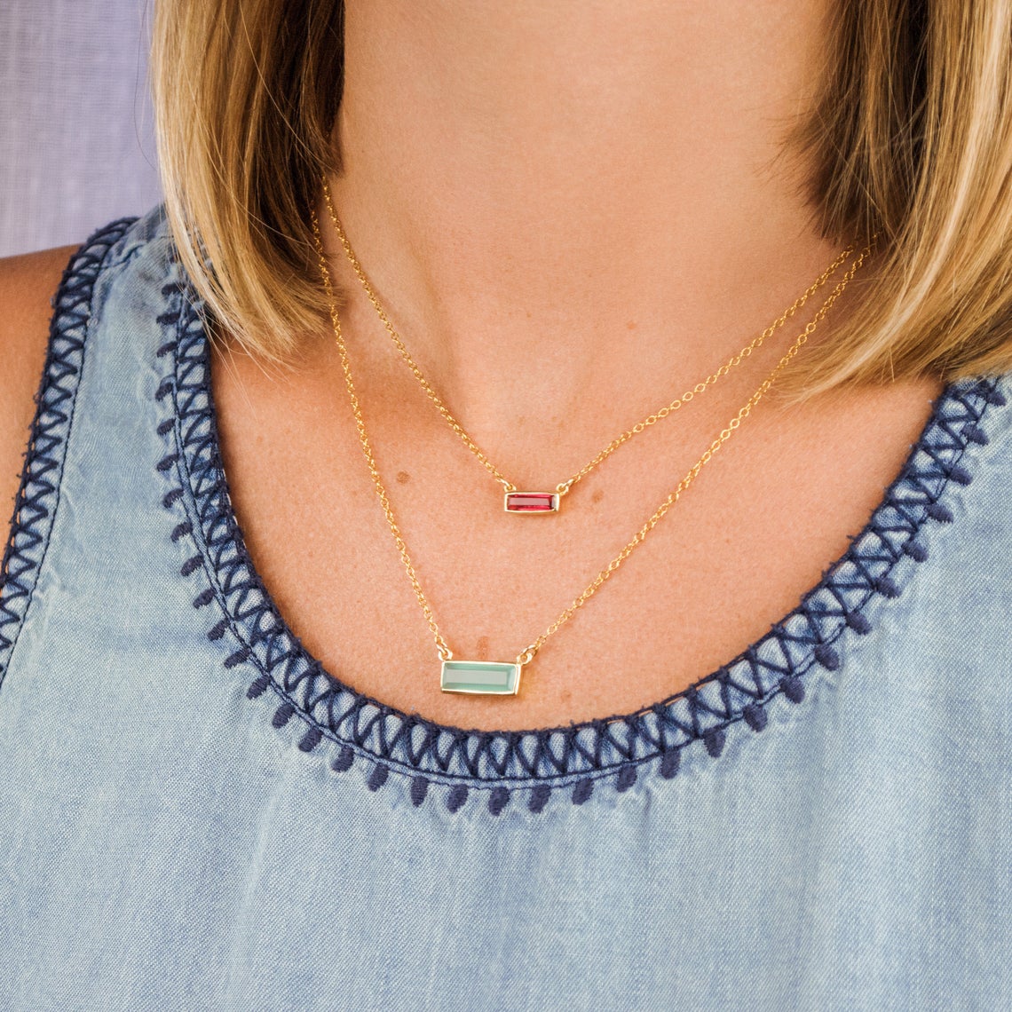 Model in blue top is stylishly layering our horizontal aqua chalcedony adira bar and tiny adira bar necklace with ruby birthstone - perfect layering necklace