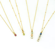 Four gold filled vertical bar necklaces displayed. Single birthstone ruby, 2 birthstones with citrine and peridot, three birthstones with aqua chalcedony, pink chalcedony and clear, and 4 birthstones Iolite, blue topaz, moonstone and clear