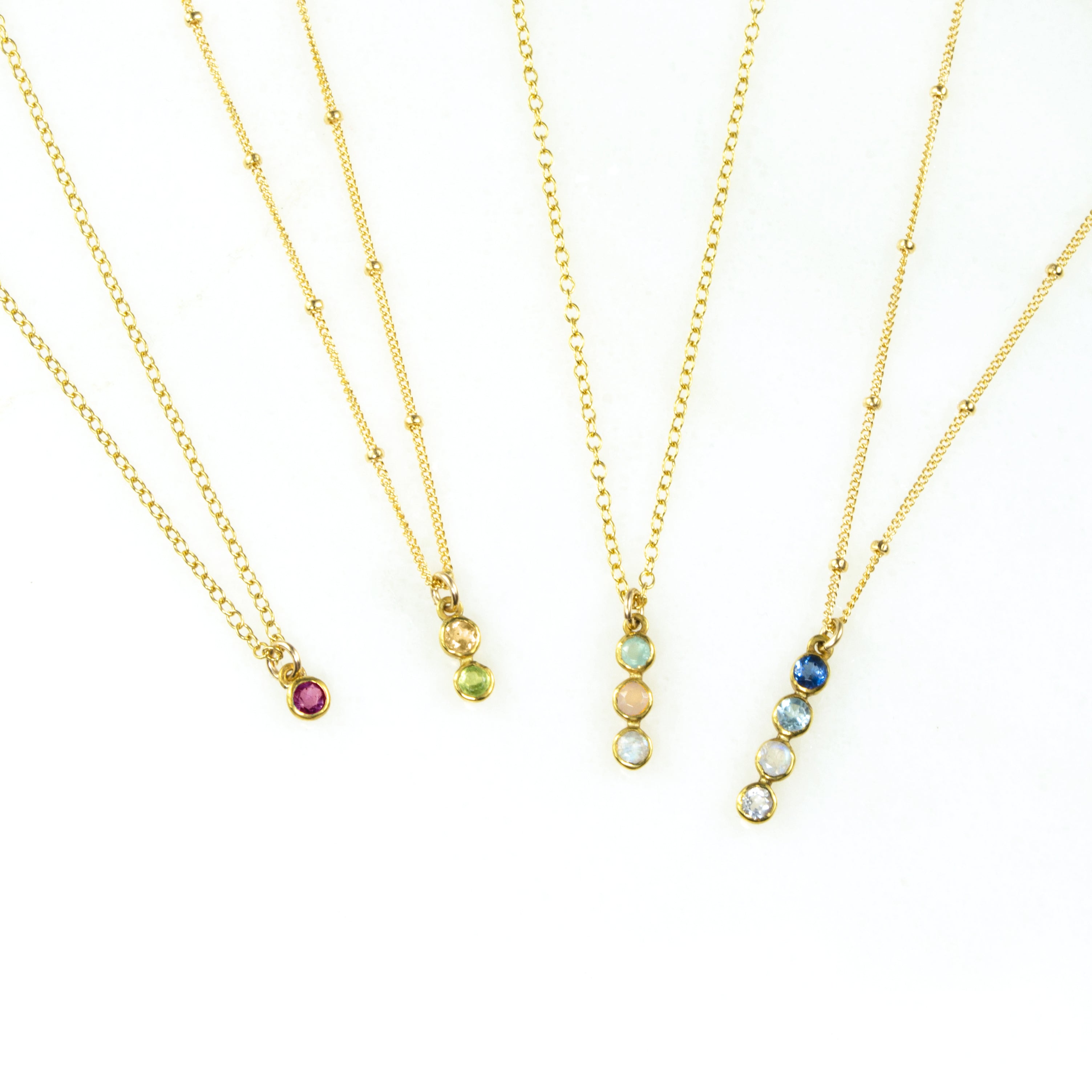 Four gold filled vertical bar necklaces displayed. Single birthstone ruby, 2 birthstones with citrine and peridot, three birthstones with aqua chalcedony, pink chalcedony and clear, and 4 birthstones Iolite, blue topaz, moonstone and clear