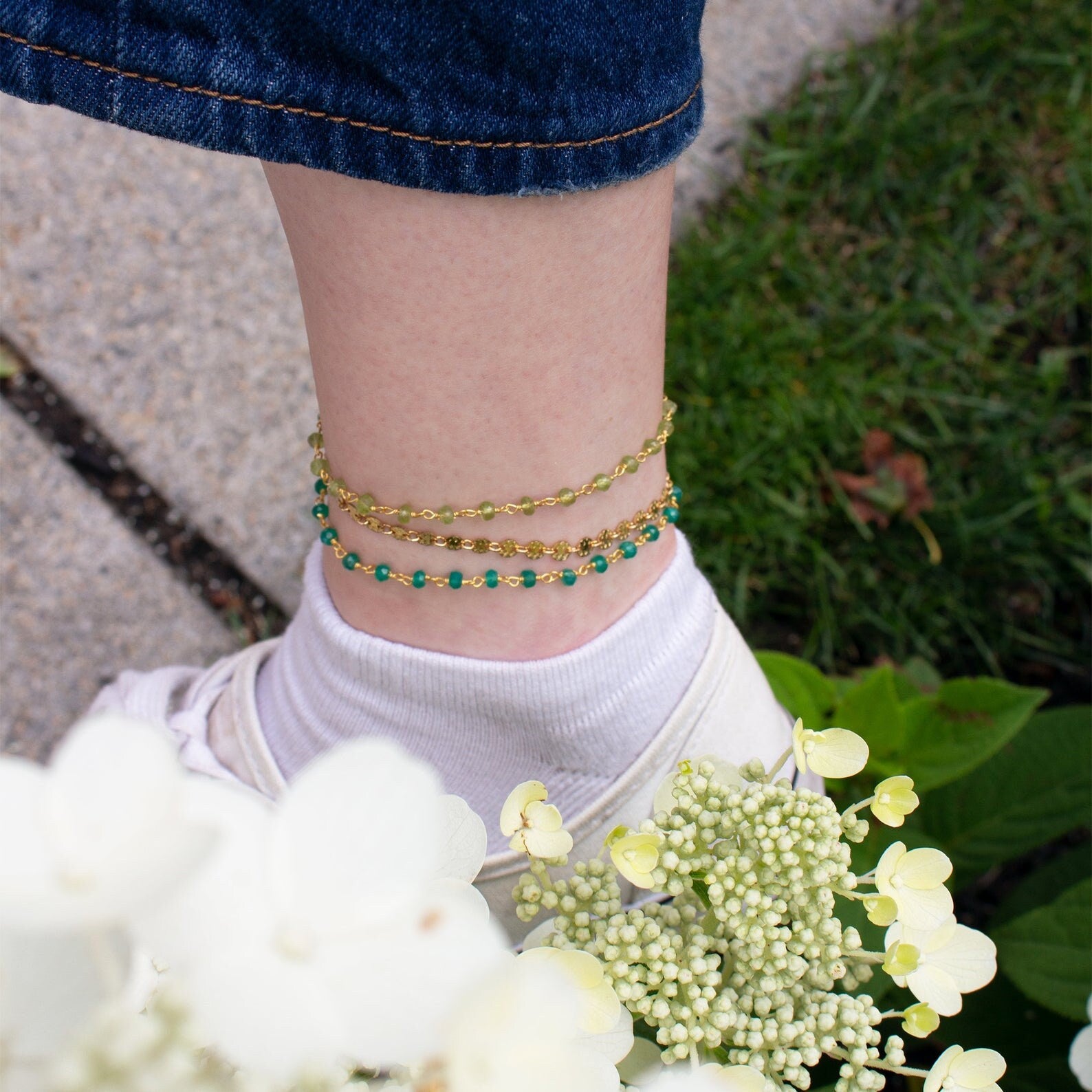 Model is fashionably sporting three anklets from our collection including gold filled wire wrapped peridot and green onyx gemstones as well as a gold filled chain anklet. 
